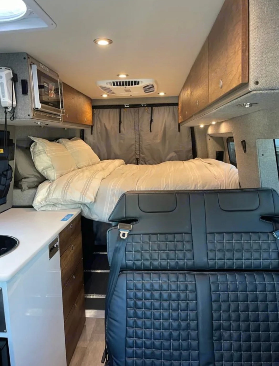 RV rental interior: cozy bed, mini kitchen, and quilted passenger seating in a well-appointed camper van.