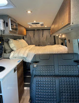 RV rental interior: cozy bed, mini kitchen, and quilted passenger seating in a well-appointed camper van.