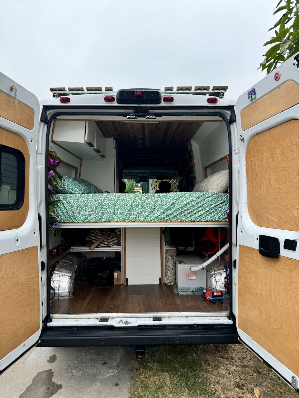 This customized camper van's interior, ideal for an rv rental, reveals a comfy bed, overhead cabinets, and utility-filled storage.