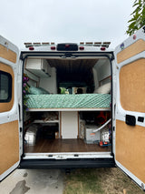 This customized camper van's interior, ideal for an rv rental, reveals a comfy bed, overhead cabinets, and utility-filled storage.