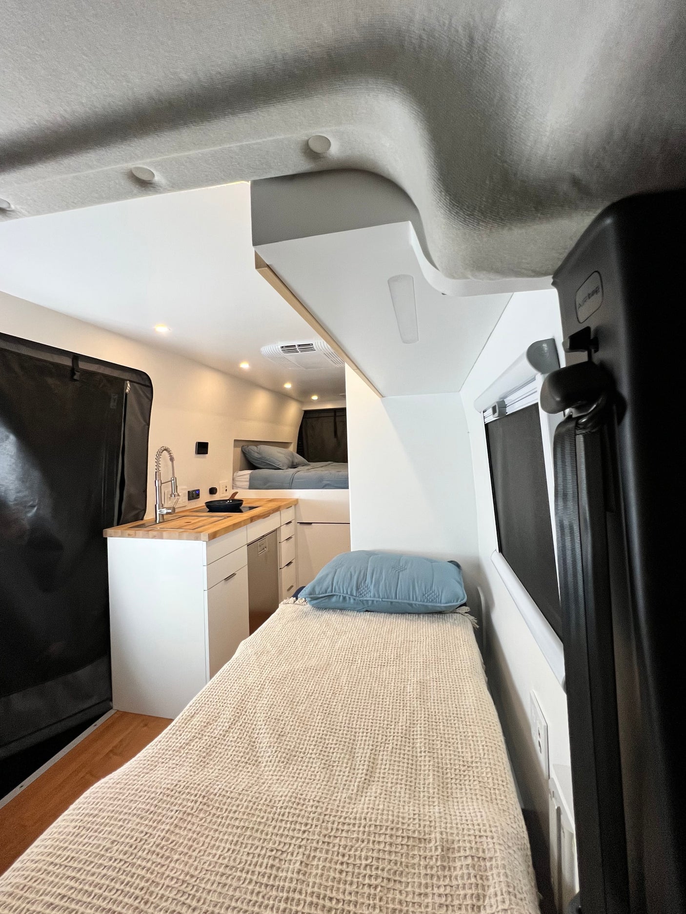 Modern RV rental interior: features a sleek kitchenette, cozy bed in foreground, and a second sleeping area for mobile adventures.
