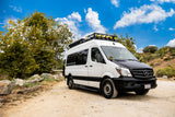 Off-road equipped white Mercedes Sprinter RV rental van parked on a dirt path, ready for adventure under a blue sky.
