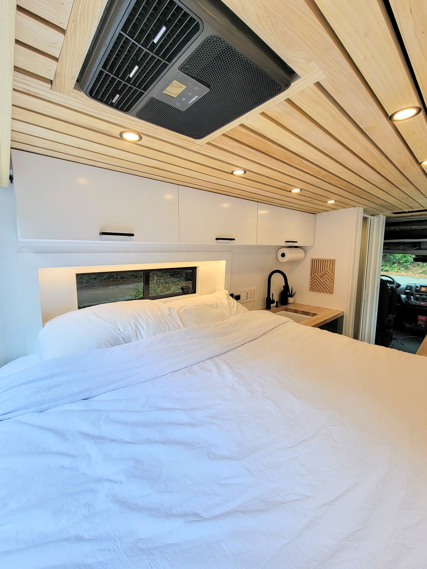 Spacious and modern RV rental interior featuring a comfy bed, compact kitchen, and stylish wood ceiling.