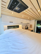 Spacious and modern RV rental interior featuring a comfy bed, compact kitchen, and stylish wood ceiling.