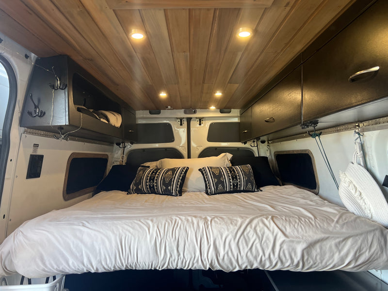 Cozy RV rental interior: a comfy bed with decorative pillows, wooden ceiling lights, & overhead storage. Ideal for road trips. — photo 2