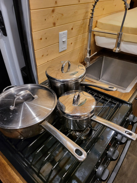 Compact RV rental kitchen with a pull-down faucet, gas stove, and organized stainless steel pots.