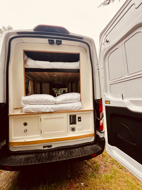 Rear view of an RV rental camper van, showing its interior with bunk beds, wooden accents, and a control panel.