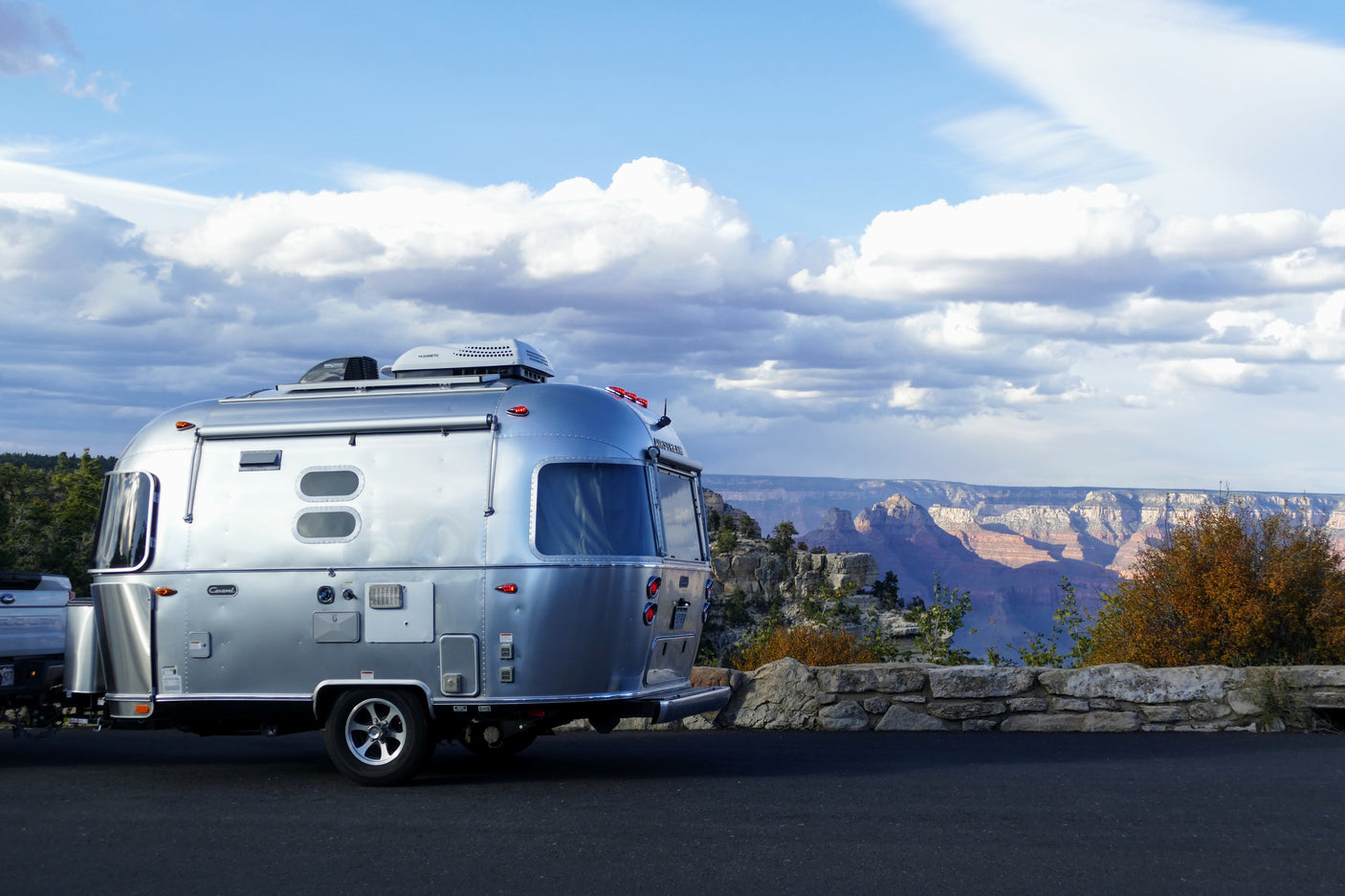 Silver Airstream RV rental offers stunning Grand Canyon views from a scenic overlook under a cloudy sky.