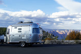 Silver Airstream RV rental offers stunning Grand Canyon views from a scenic overlook under a cloudy sky.