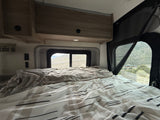 Cozy bed in an RV rental, offering scenic mountain views through the window. Overhead cabinets and reading light add comfort.