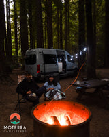 RV rental adventure: Couple by campfire at a forest campsite with their campervan, under string lights.