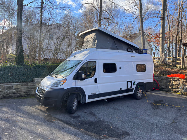 This white pop-top campervan, perfect for an RV rental adventure, is parked on a sunny driveway, connected to shore power.