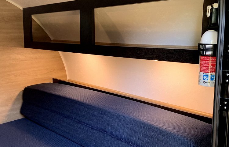 Inside an RV rental: blue bed, overhead cabinets, under-cabinet lighting, and a fire extinguisher for safety. — photo 14