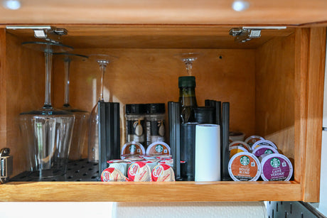 RV rental kitchen cabinet, neatly stocked with K-Cups, coffee creamer, wine glasses, and cooking essentials.