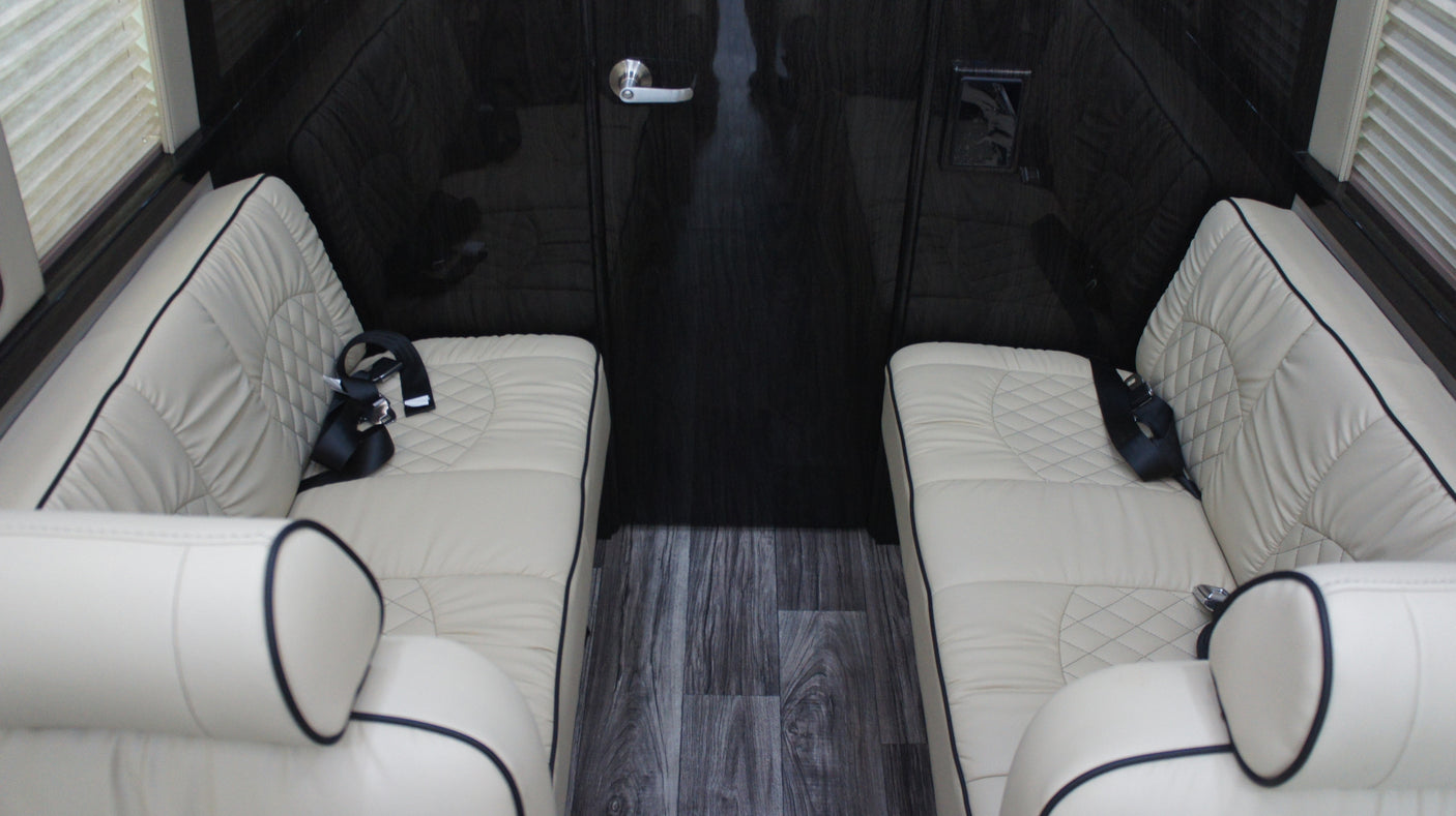 Luxurious RV rental interior features cream quilted leather seating, dark wood walls, & floor.