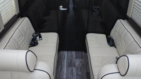Luxurious RV rental interior features cream quilted leather seating, dark wood walls, & floor.