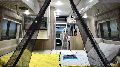 This RV rental features a comfortable sleeping area with yellow bedding & mosquito net, compact kitchen, and views from its windows.