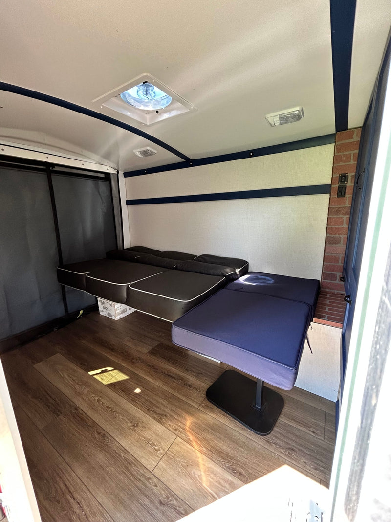 Inside an RV rental, showing convertible black and navy seating/beds on wood laminate flooring. Features a ceiling fan and interior lights. — photo 3
