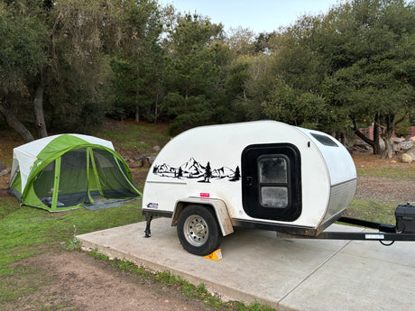 White teardrop RV rental and green tent set up at a scenic campsite for an outdoor escape.