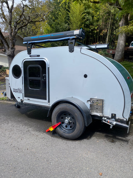 This white teardrop camper, great for an RV rental, features a rooftop road shower for comfortable outdoor camping.
