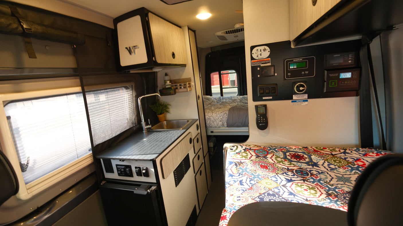 Inside a modern RV rental: compact kitchen, multi-functional control panel, and cozy sleeping area for adventurers.