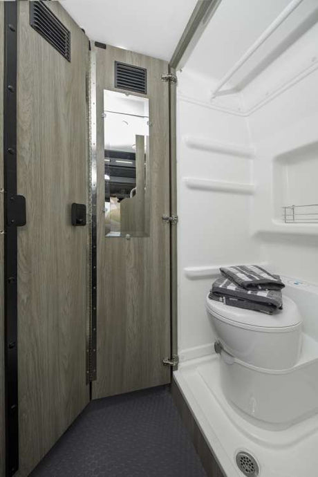 This RV rental offers a compact bathroom with a toilet, shower, and a mirror on the wood-grain interior panel.