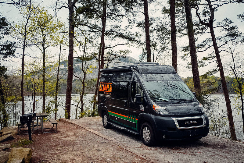 Black Scamper RV rental at a scenic lakeside campsite with a picnic table, surrounded by trees and mountains. — photo 17