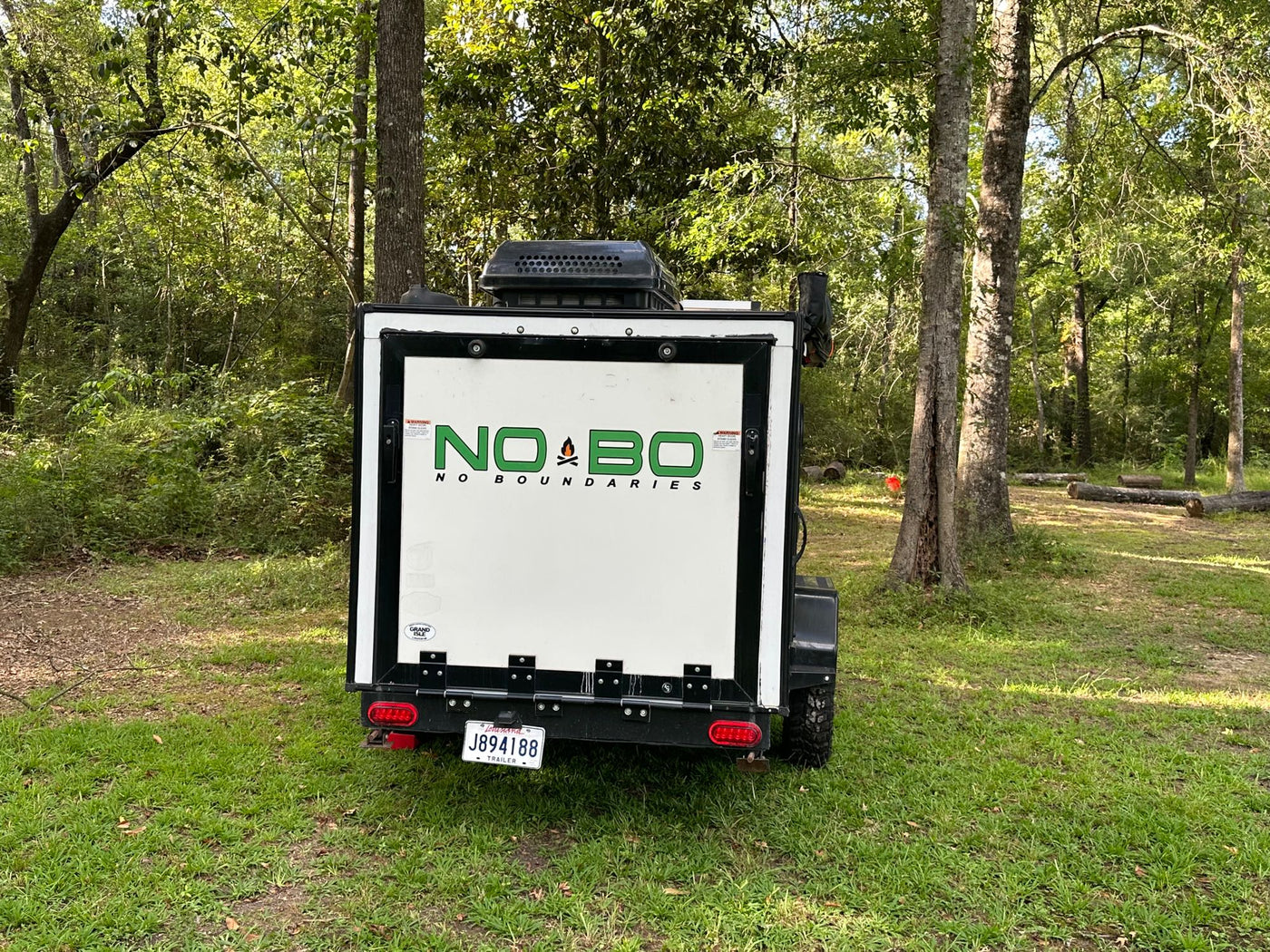 White NO BO camper trailer for RV rental adventures, parked in a lush, green forest campsite in Louisiana. — photo 7