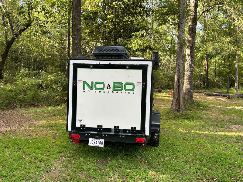 White NO BO camper trailer for RV rental adventures, parked in a lush, green forest campsite in Louisiana. — photo 7