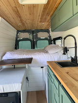  surrounded by bare trees under a clear blue sky.|RV rental: Cozy camper van interior with a bed
