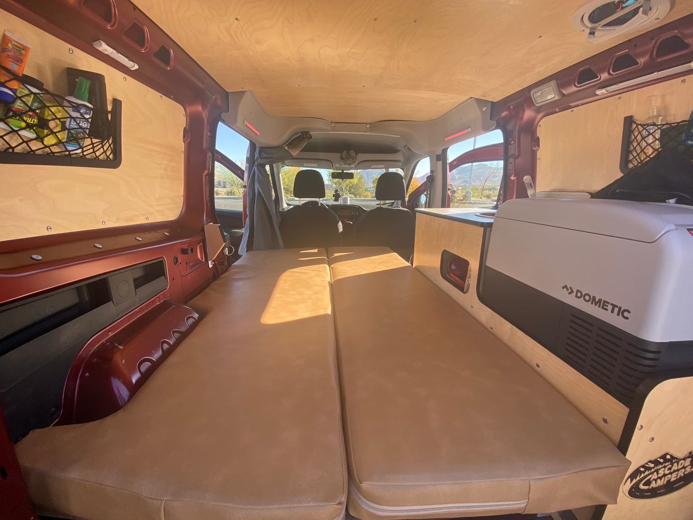 Cozy rv rental van conversion with a bed, cooler, and wood paneling, ready for adventure.
