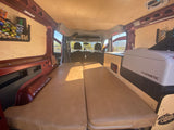 Cozy rv rental van conversion with a bed, cooler, and wood paneling, ready for adventure.