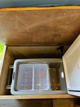 RV rental: Portable RV refrigerator with internal baskets in an open wooden storage compartment, ready for trips.