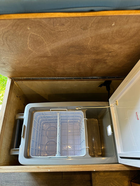 RV rental: Portable RV refrigerator with internal baskets in an open wooden storage compartment, ready for trips.