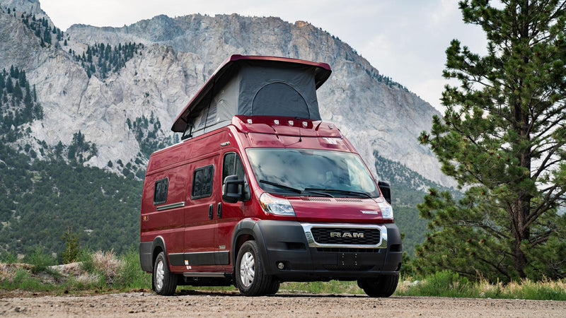 Red pop-top camper van parked on a dirt road with mountains & trees.|Winnebago RV rental interior: compact kitchen — photo 1