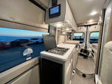 Interior of an rv rental, featuring a modern kitchenette, control panel, and an outside view from the window.