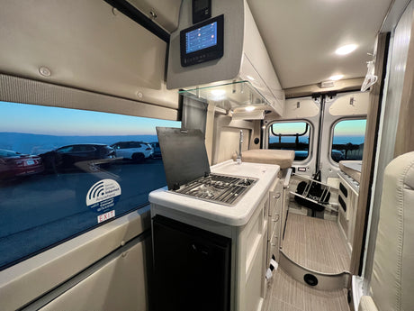 Interior of an rv rental, featuring a modern kitchenette, control panel, and an outside view from the window.