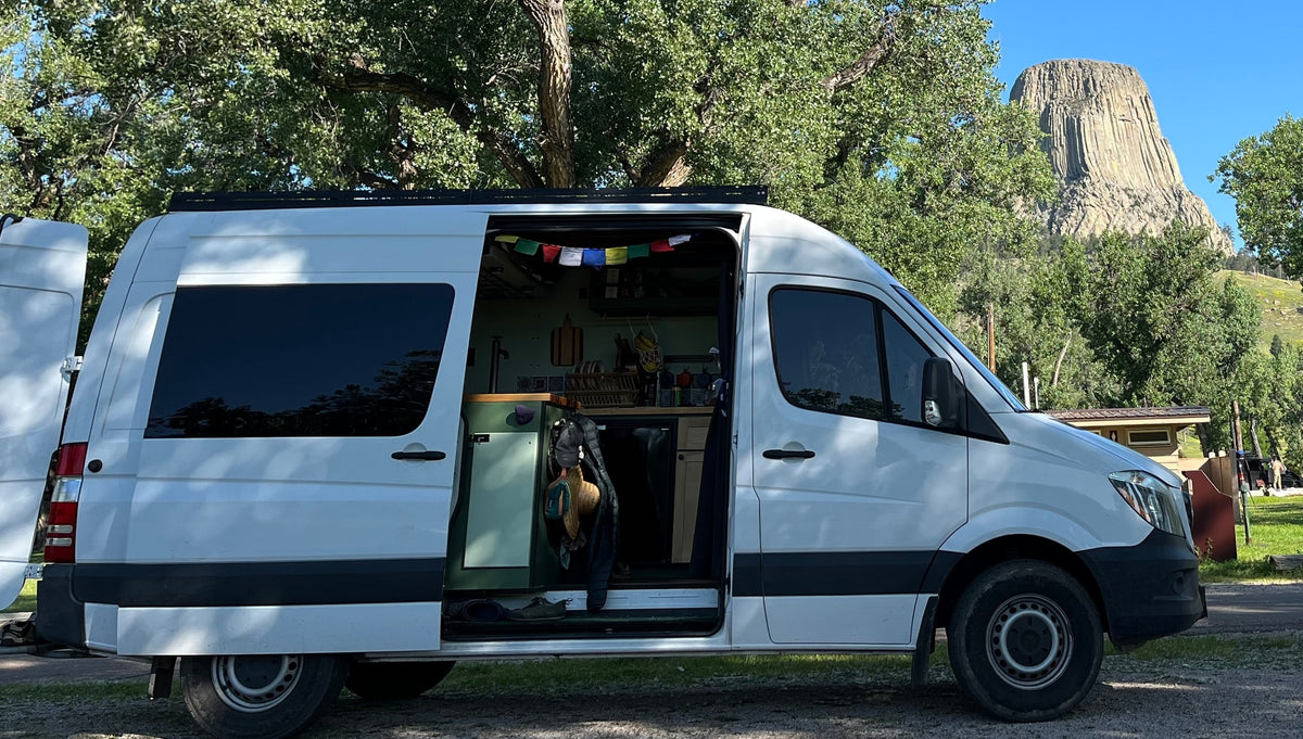 Exploring Devils Tower in a white RV rental camper van. Open side door shows cozy interior