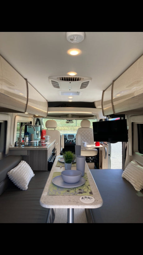 Spacious RV rental interior featuring a full kitchen, dining table, and cozy lounge area that converts to a bed.