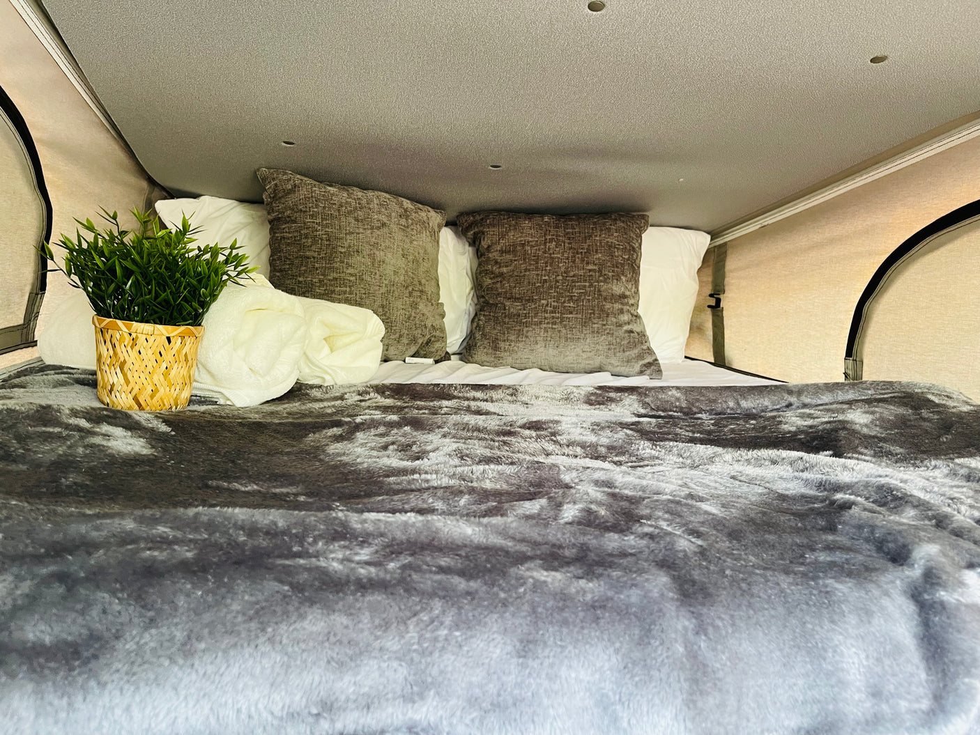 Experience comfort in this RV rental! Plush grey bedding, white pillows, and a touch of green make this camper bed inviting.