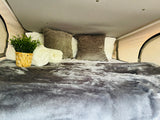 Experience comfort in this RV rental! Plush grey bedding, white pillows, and a touch of green make this camper bed inviting.