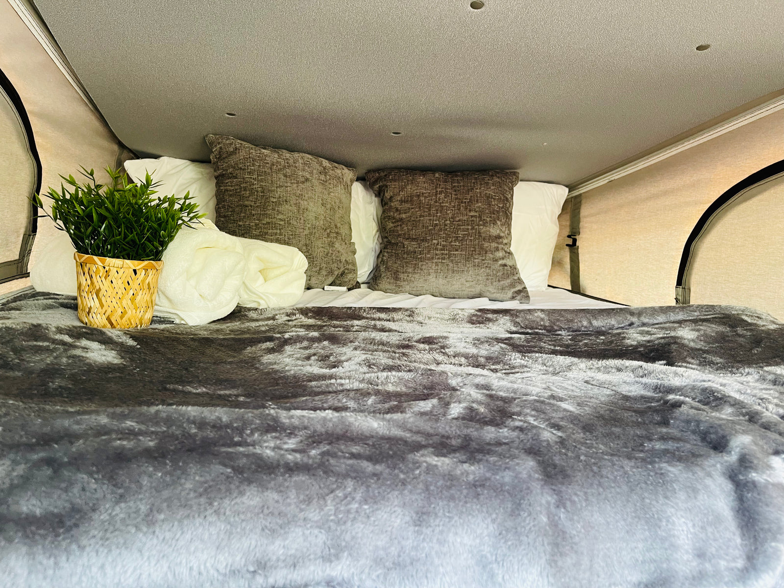 Experience comfort in this RV rental! Plush grey bedding, white pillows, and a touch of green make this camper bed inviting.