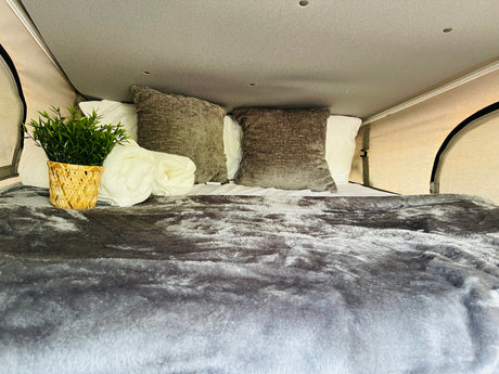 Experience comfort in this RV rental! Plush grey bedding, white pillows, and a touch of green make this camper bed inviting.