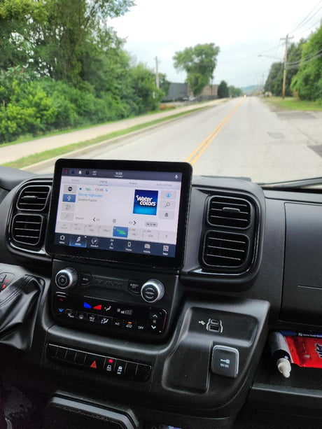Inside an RV rental: dashboard with a large touchscreen infotainment system playing music, with the road ahead visible.