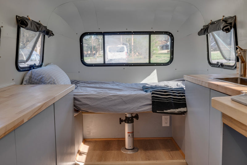An RV rental's interior shows a striped bed, wooden counters with a sink, and windows, offering a cozy, functional space. — photo 4