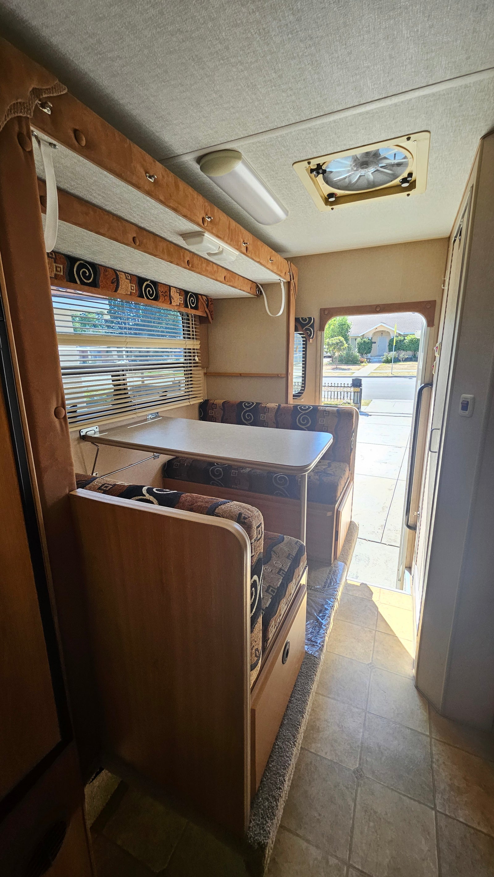 Explore this RV rental's interior: a cozy dinette with patterned cushions, a large window with blinds, and practical tile flooring.