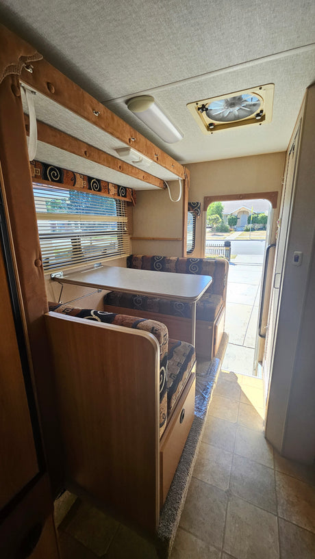 Explore this RV rental's interior: a cozy dinette with patterned cushions, a large window with blinds, and practical tile flooring.
