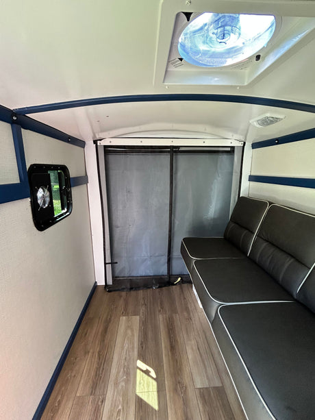 RV rental interior: black sofa, wood floor, blue trim, window fan, and ceiling vent. A bright and functional space.
