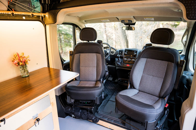 Inside an RV rental: Front cabin with two seats, dashboard, and a wooden table on the left with dried flowers. — photo 19