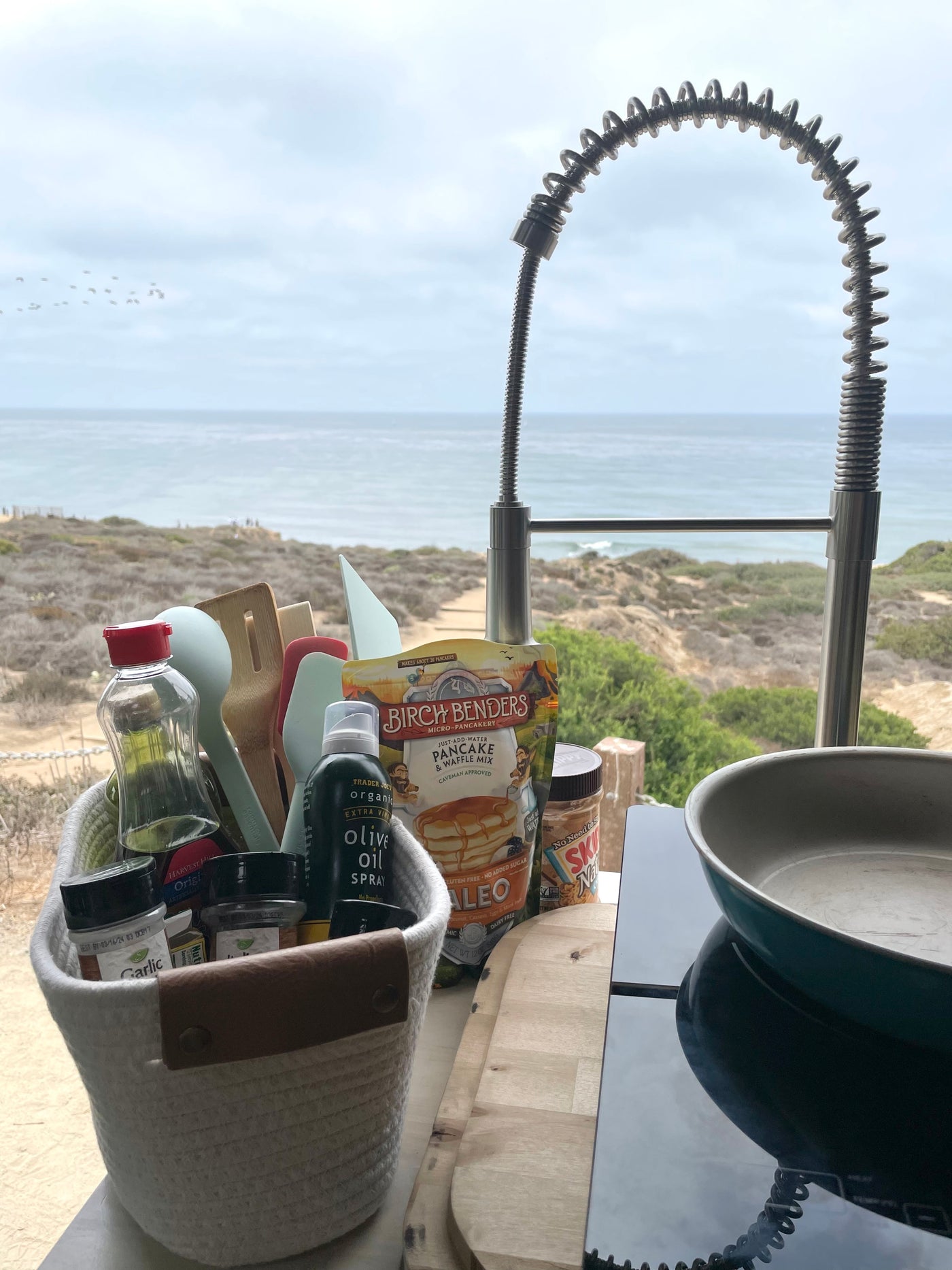 An RV rental's compact kitchen setup, with a pan, pancake mix, and olive oil spray, overlooks a stunning ocean view. — photo 12